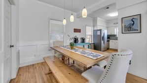 Una cocina moderna con armarios blancos, una mesa de comedor de madera e iluminación colgante.