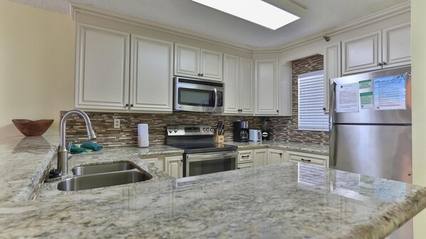 A kitchen with white cabinets, a stainless steel refrigerator, a microwave, a stove, and a sink. - Destin on the Gulf 302 (Destin)