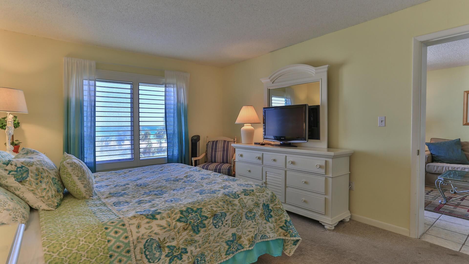 A bedroom with a bed, a dresser with a TV, a chair, and a window with curtains.