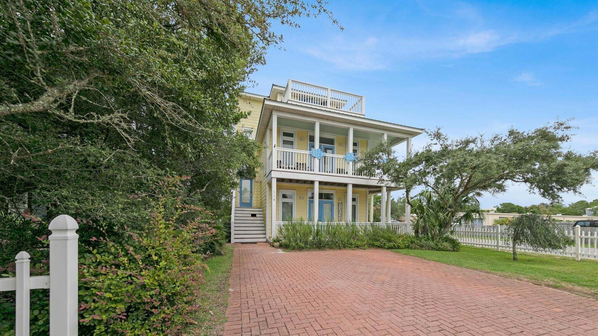 A two-story building with a balcony, a brick pathway leading to the entrance, and a white picket fence.