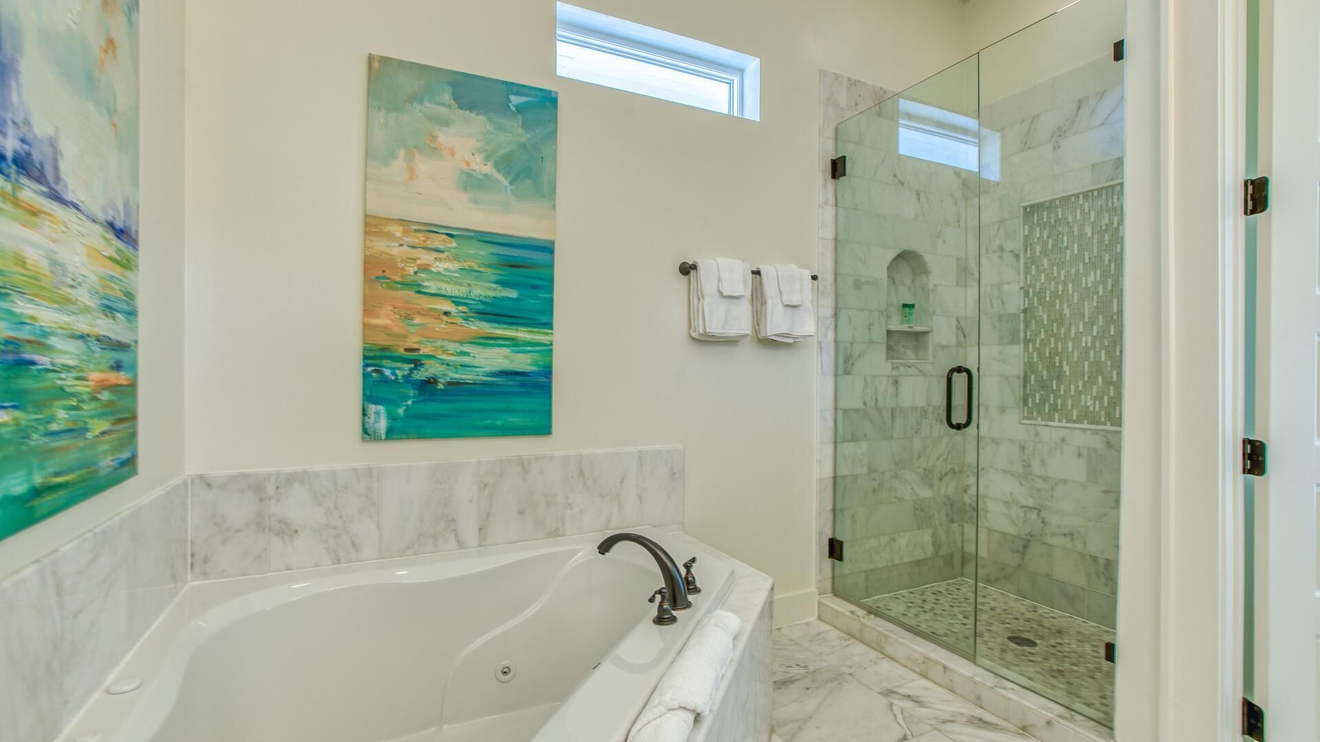 A modern bathroom with a freestanding bathtub, a glass-enclosed shower, and two large paintings on the walls.