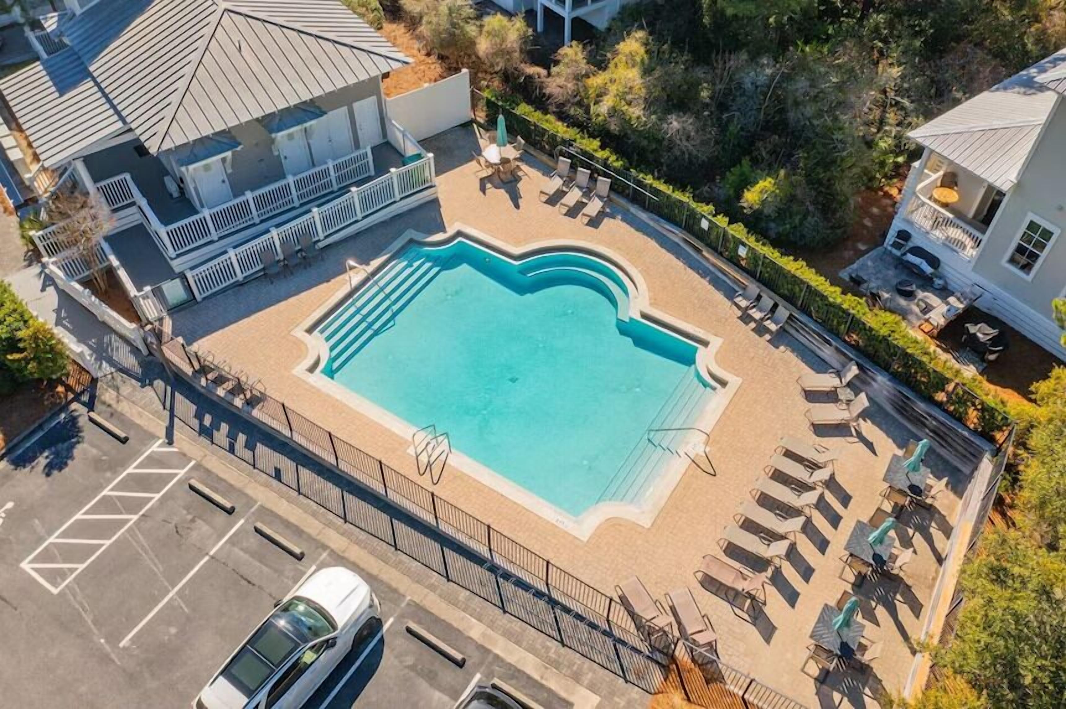 An aerial view of a property with a swimming pool, lounge chairs, and a covered patio area.