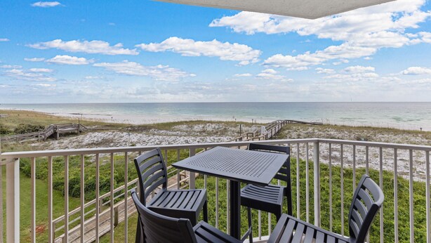 Een balkon met een tafel en stoelen, uitkijkend op een strand.