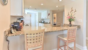 A kitchen with a granite countertop, two white chairs, and a vase with flowers. - Destin Towers 143 (Destin)