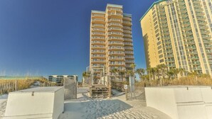A high-rise hotel with multiple balconies, located near a beach with a sandy walkway leading to the entrance. - Destin Towers 143 (Destin)