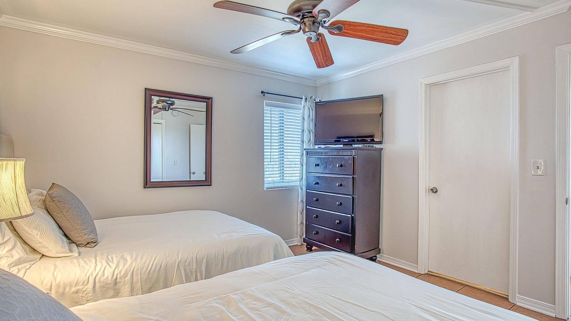 A bedroom with two beds, a dresser, a ceiling fan, a mirror, and a door.