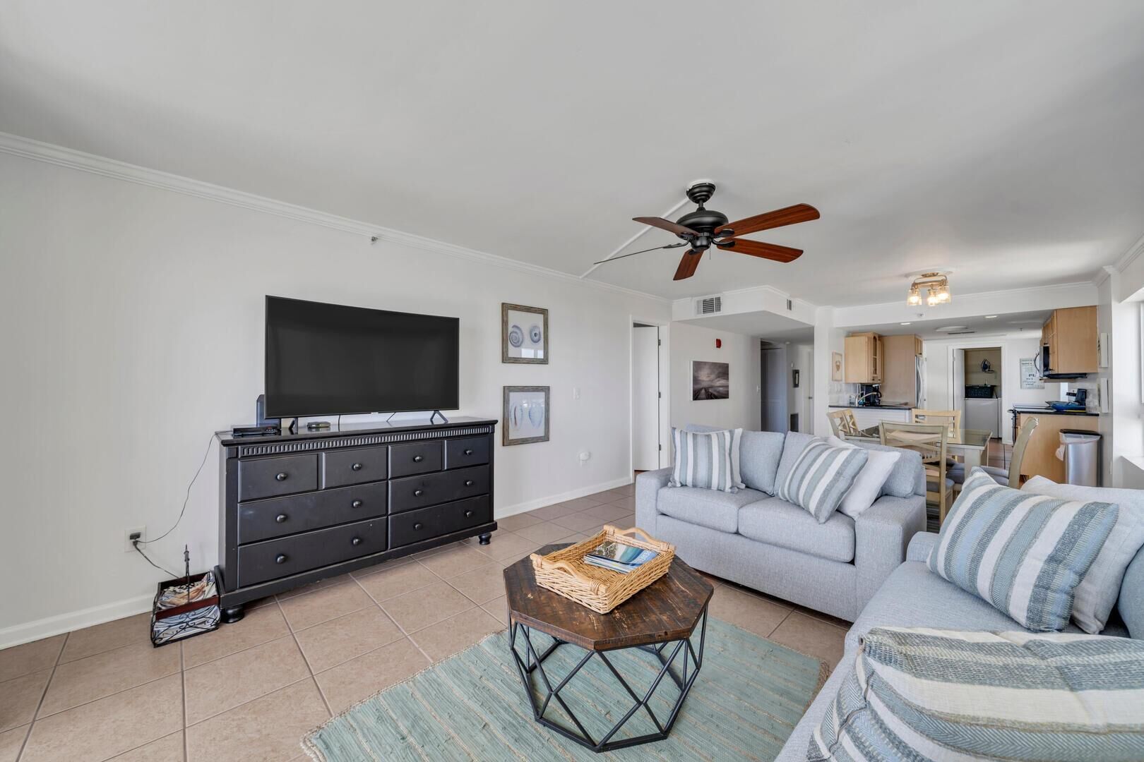 A living room with a flat-screen TV, a black dresser, a gray sofa, and a ceiling fan.