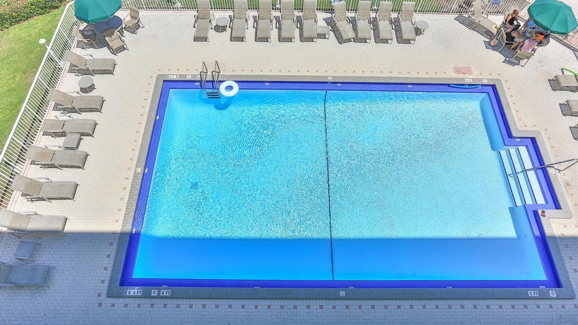 A rectangular swimming pool with a blue border, surrounded by lounge chairs and umbrellas.