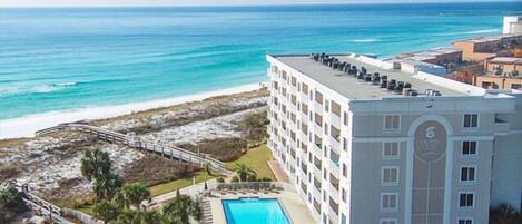 A hotel with a pool, beachfront view, and a beach area with palm trees.