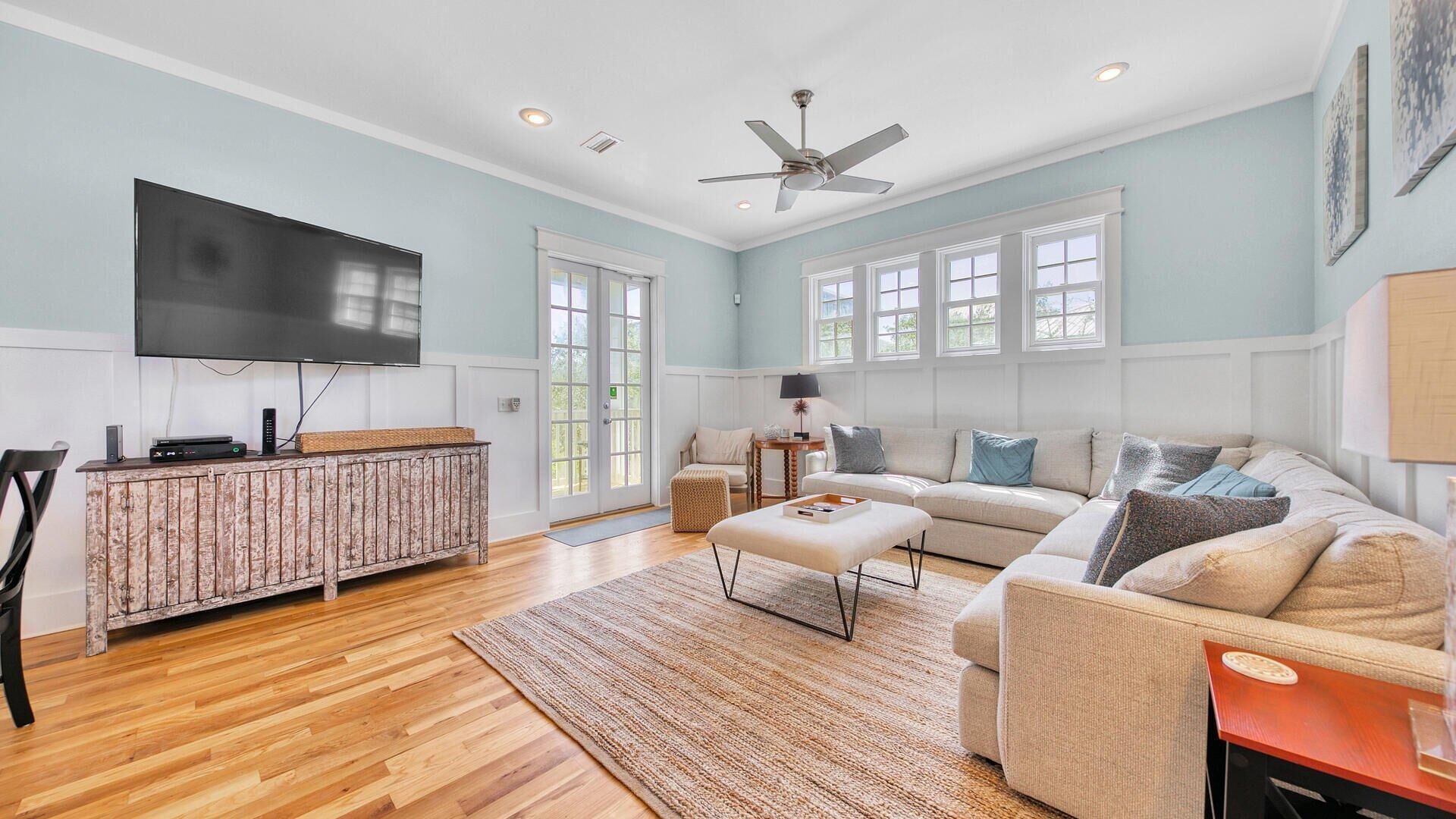 A spacious living room with a large flat-screen TV, a wooden cabinet, a sofa set, and a ceiling fan.