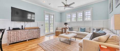 A spacious living room with a large flat-screen TV, a wooden cabinet, a sofa set, and a ceiling fan.