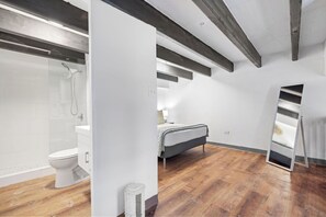 A modern bathroom with a glass shower enclosure, a white toilet, and a wooden floor.