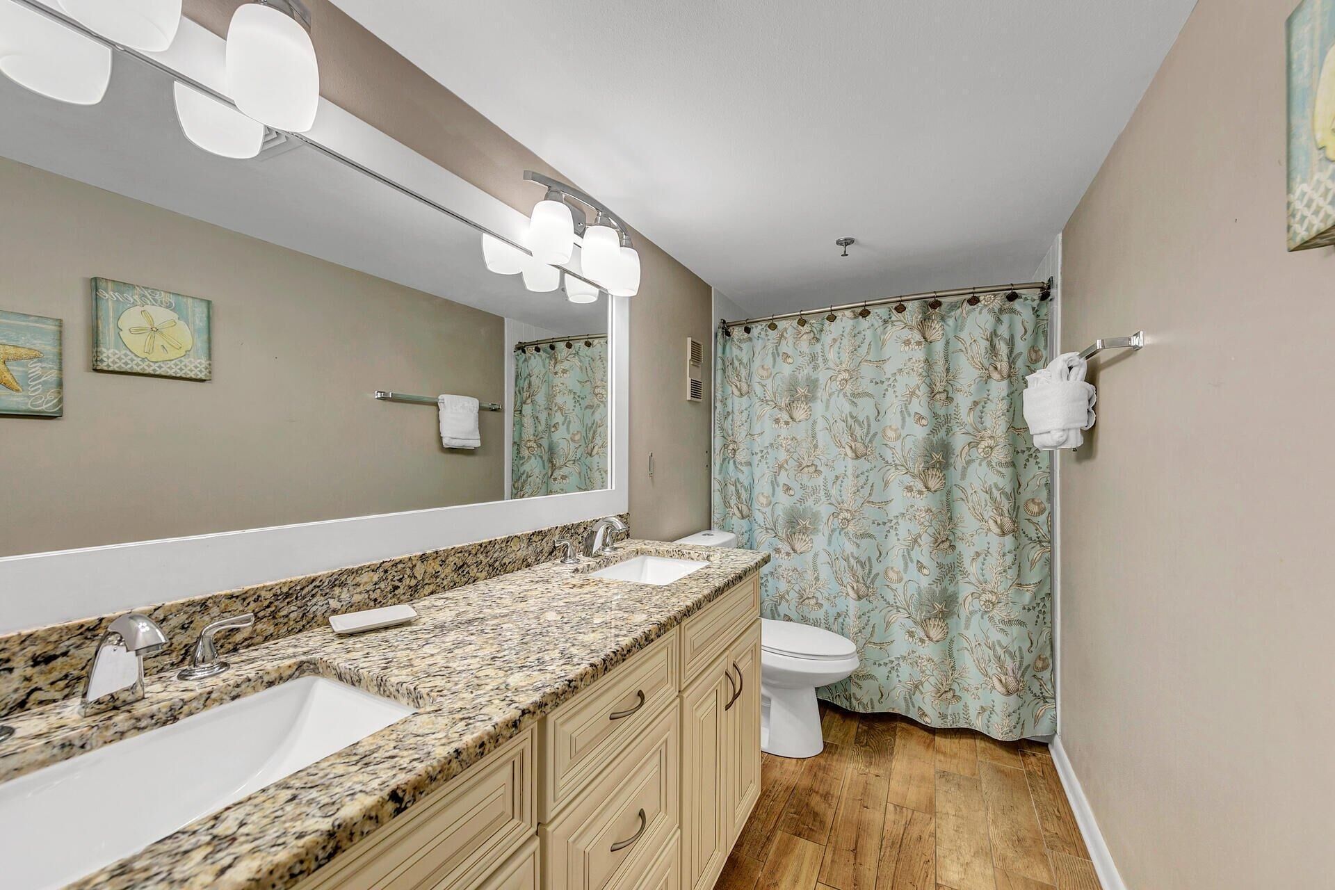 A bathroom with a granite countertop sink, a toilet, and a shower curtain with a floral pattern.