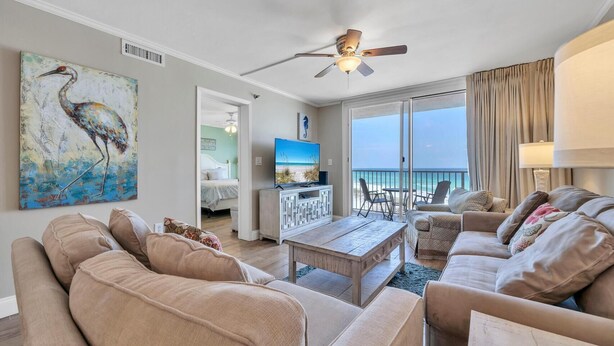 A living room with a large sofa, a coffee table, and a TV. There is a painting of a bird on the wall and a balcony with a view of the ocean. - Destin on the Gulf 702 (Destin)