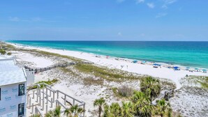 A beach view with a white building, a wooden deck, and a clear blue sky. - Destin on the Gulf 702 (Destin)