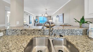 A kitchen with granite countertops, stainless steel sink, and a view to the living area. - Destin on the Gulf 702 (Destin)