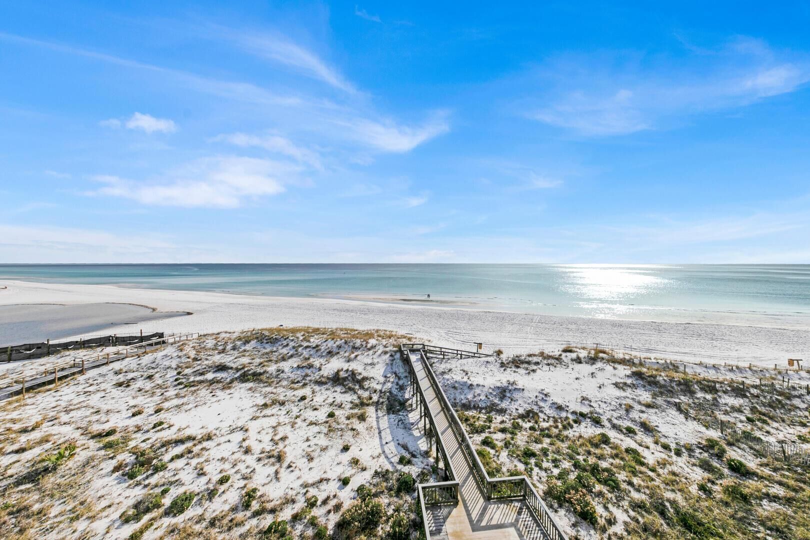 A beach with a wooden boardwalk leading to the water, sandy dunes, and a clear sky.
