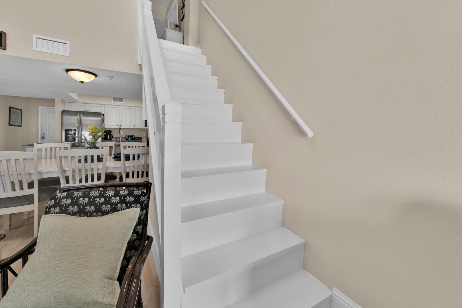 Eine Treppe führt zu einem Essbereich mit weißen Wänden und einer Küche im Hintergrund.