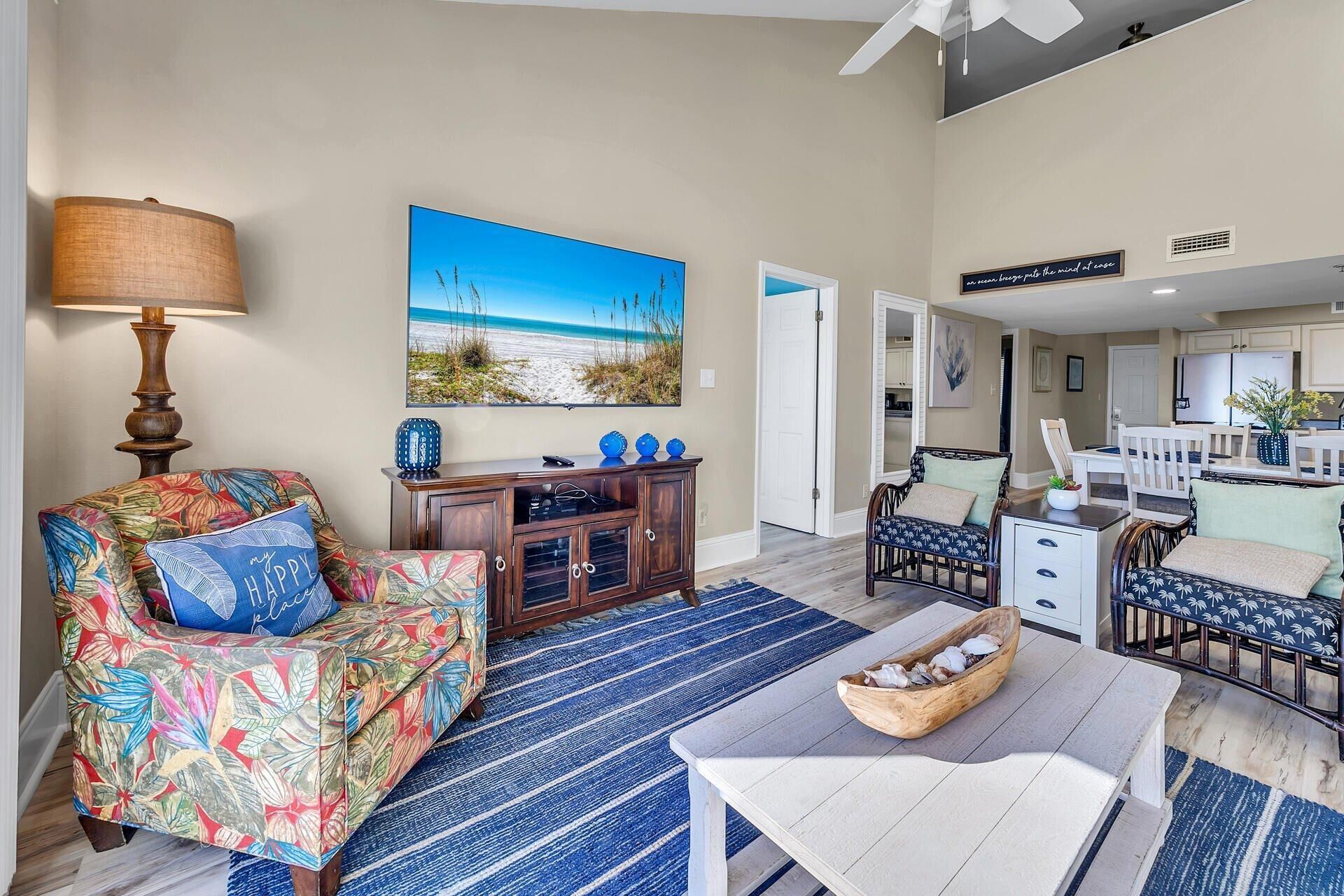 Un salon avec un canapé aux motifs évoquant la plage, un meuble en bois et un grand tableau représentant un paysage de plage.