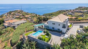 A modern house with a swimming pool, surrounded by lush greenery and a view of the sea. - Sunshine Deluxe B by Madeira Sun Travel (Ponta do Sol)