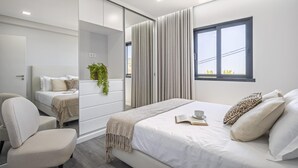 A modern bedroom with a large bed, a bedside table, a chair, a mirror, and a window with curtains. - Sunshine Deluxe B by Madeira Sun Travel (Ponta do Sol)
