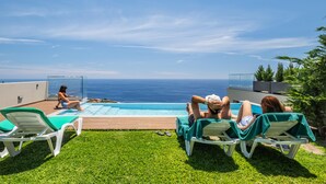A poolside area with lounge chairs, a swimming pool, and a view of the ocean. - Sunshine Deluxe C by Madeira Sun Travel (Ponta do Sol)