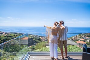 A couple standing on a balcony overlooking a coastal view.