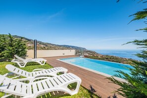A swimming pool with lounge chairs and a view of the sea.