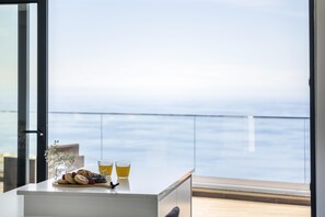 A breakfast table with pastries, a glass of juice, and a vase with flowers, overlooking a balcony with a view of the sea. - Sunshine Deluxe C by Madeira Sun Travel (Ponta do Sol)