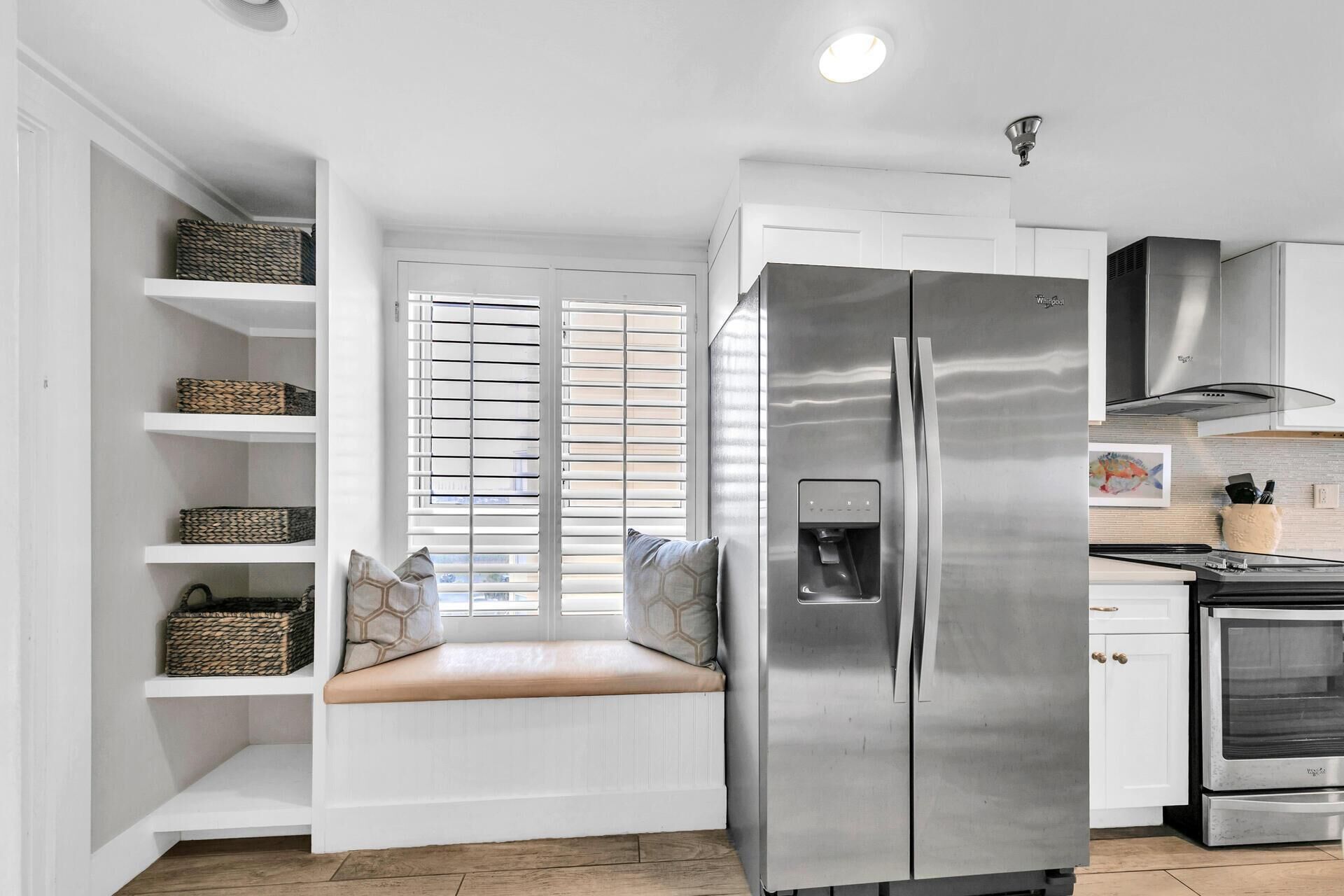 A kitchen with a built-in bench, white cabinetry, a stainless steel refrigerator, and a stove.