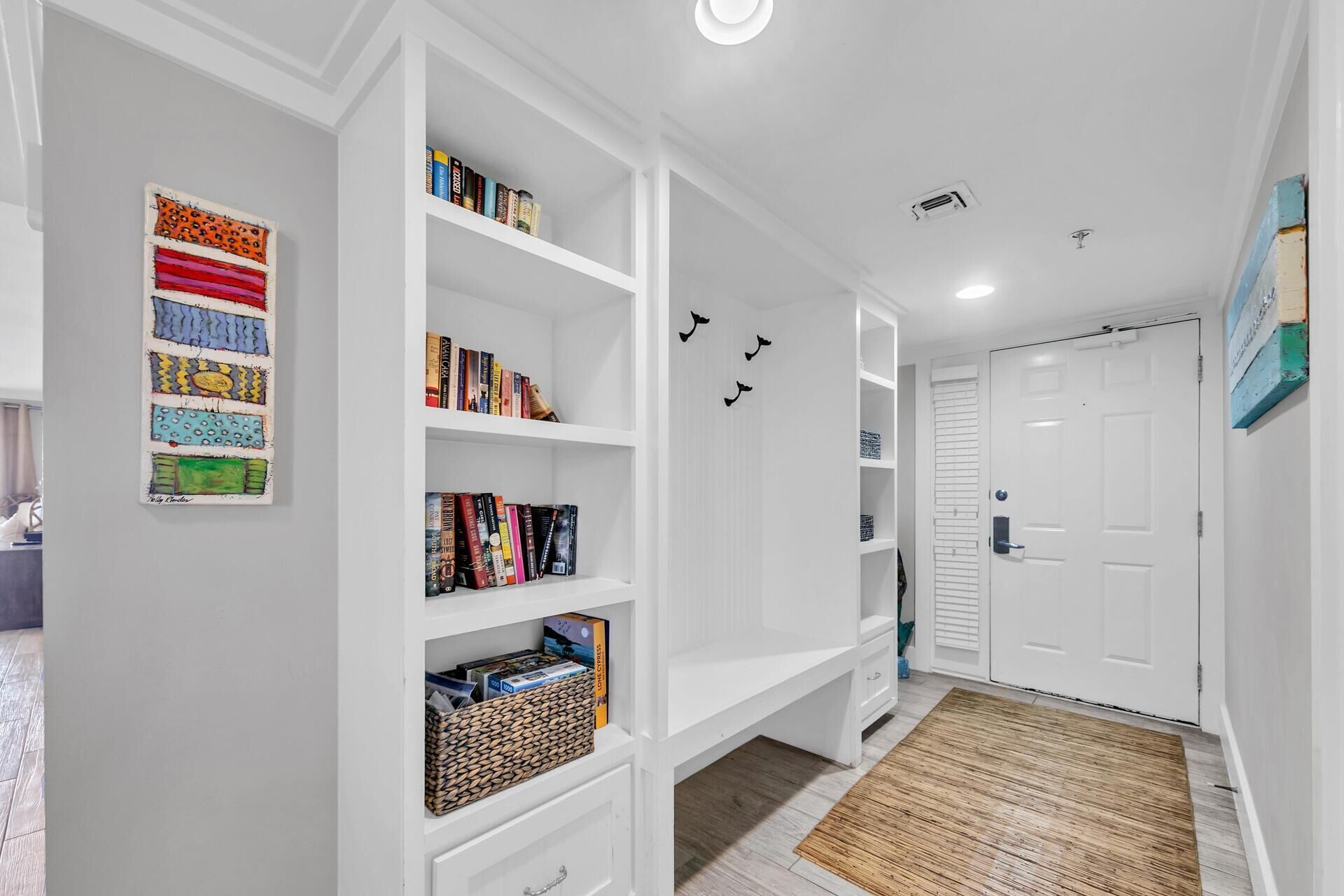 A hallway with white shelving units, a door, and a patterned rug.