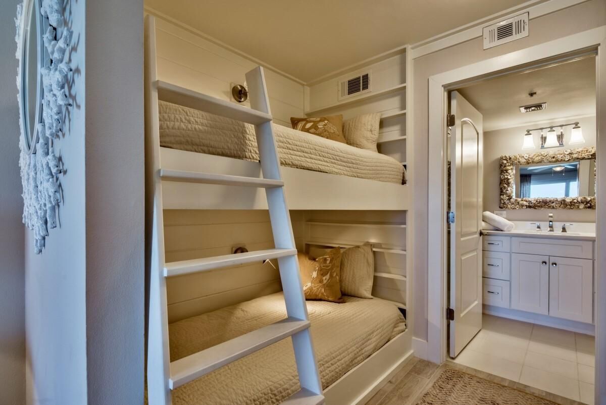 Een slaapkamer met stapelbedden, een ladder, een badkamer met spiegel en wastafel, en een klein opbergruimte.