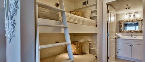 Een slaapkamer met stapelbedden, een ladder, een badkamer met spiegel en wastafel, en een klein opbergruimte.