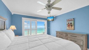 Een slaapkamer met een bed, een plafondventilator, een televisie, een dressoir en uitzicht op de oceaan.