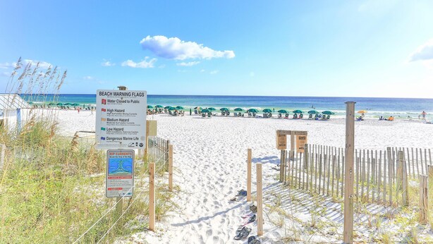 Une plage bordée d’une clôture en bois, un panneau indiquant les différents drapeaux de signalisation et une vue sur l’océan.