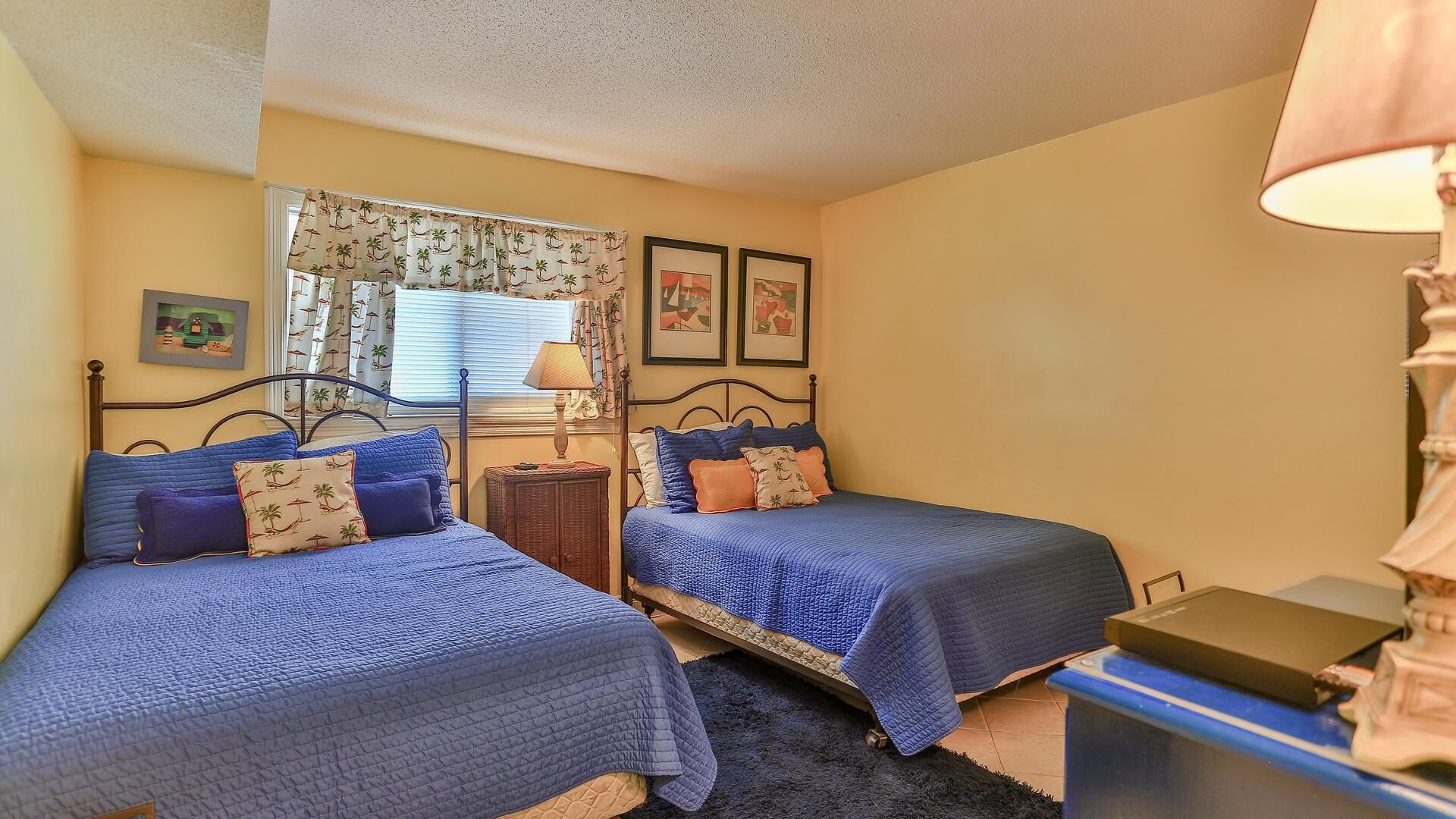 A bedroom with two beds, a nightstand, a lamp, and framed pictures on the wall.