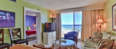A hotel room with a balcony, a TV, a sofa, and a dining table.