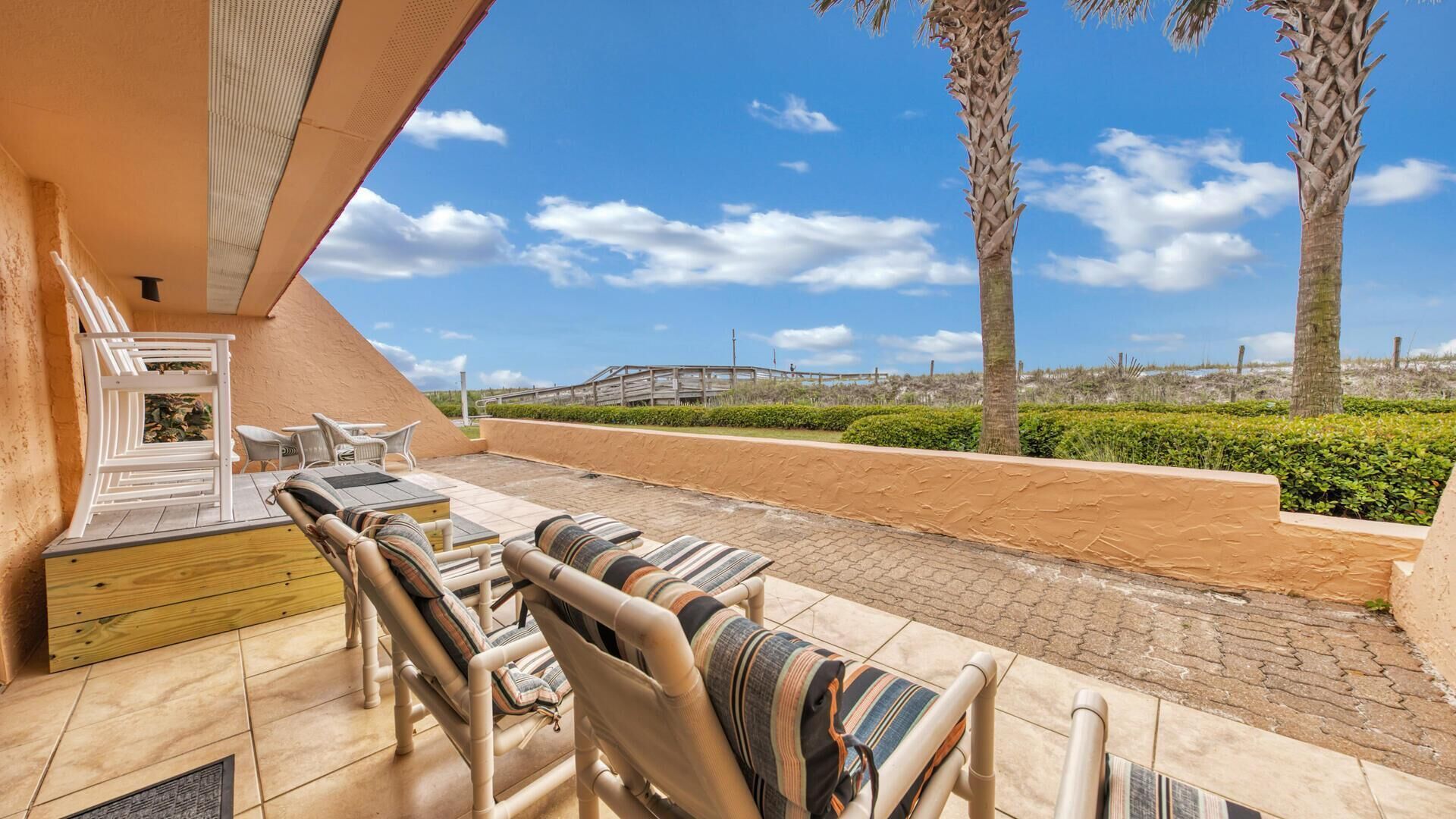 An outdoor seating area with lounge chairs and a wooden table, overlooking a landscaped garden and a distant bridge.