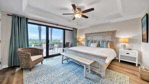 Un dormitorio con una cama grande, un ventilador de techo, una mesita de noche, un banco y vistas al exterior mediante una puerta corrediza.