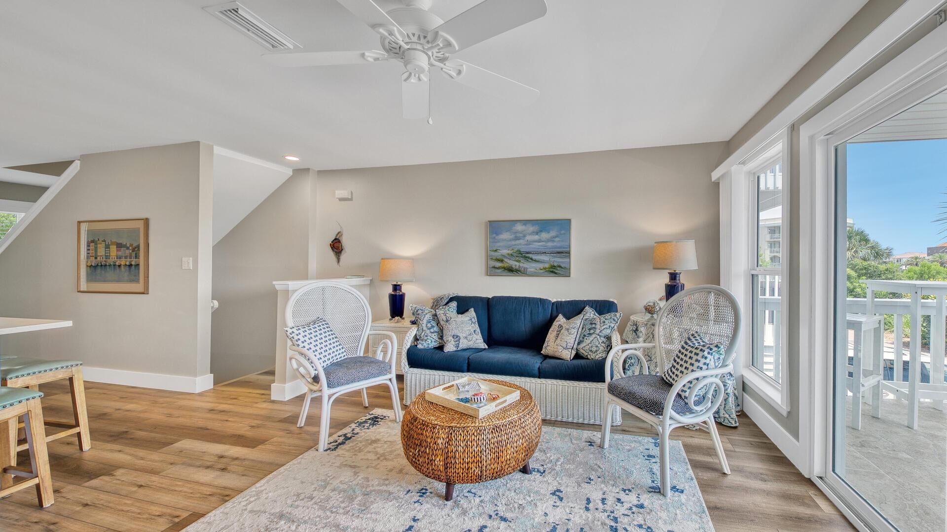 Un salon spacieux avec un canapé bleu, des fauteuils en osier blancs et un ventilateur de plafond.