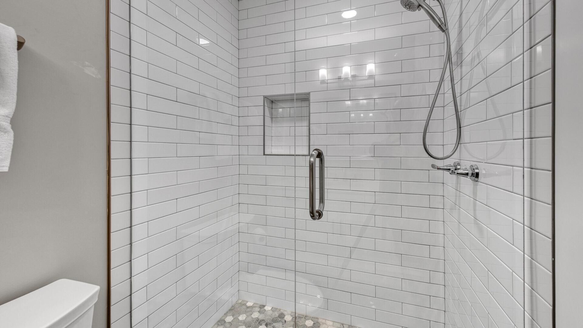 A modern shower with a handheld showerhead and a glass-enclosed corner sink.