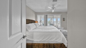 Habitación de hotel con una cama grande, ventilador de techo y vistas al exterior por las ventanas.