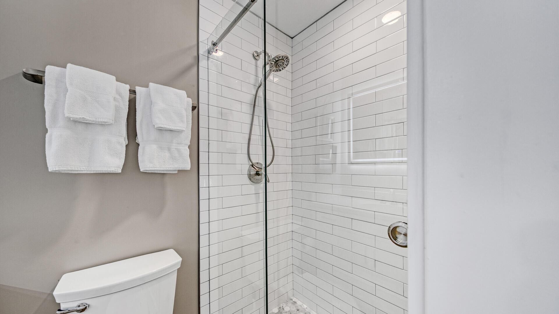 A modern bathroom with a glass-enclosed shower, white tiled walls, and a toilet.