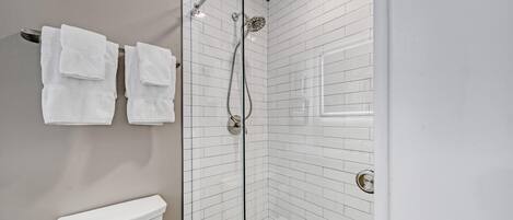 A modern bathroom with a glass-enclosed shower, white tiled walls, and a toilet.