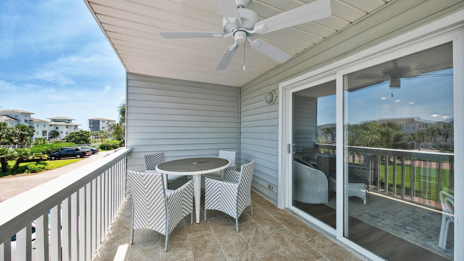 A covered balcony with a table and chairs, a ceiling fan, and a sliding glass door leading to a patio.