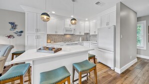 Una cocina moderna con armarios blancos, una isla central con taburetes, un refrigerador e iluminación colgante.