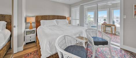 A bedroom with a large bed, two nightstands, a ceiling fan, a window with blinds, and a view of the outside.