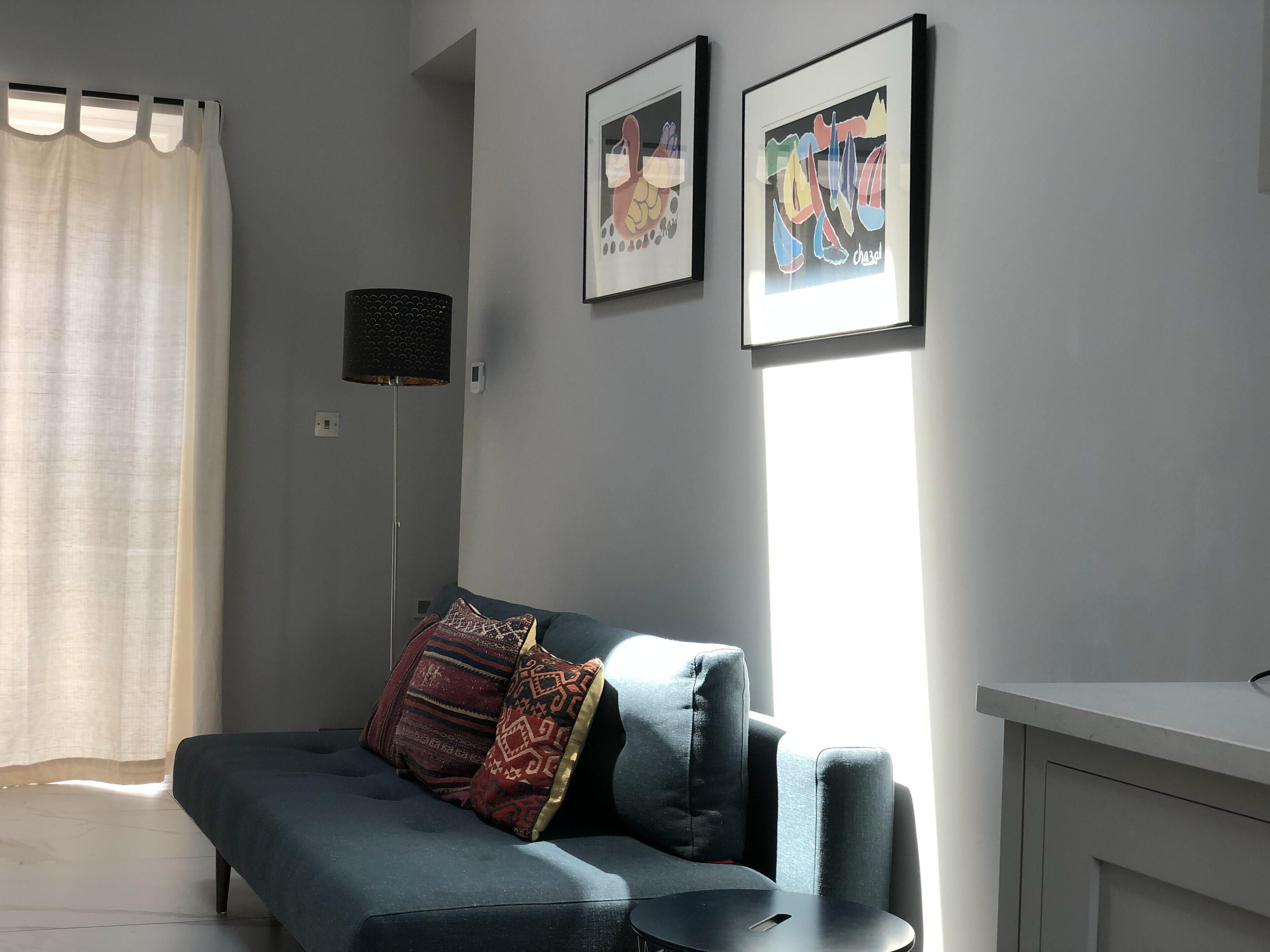 A modern living room with a sofa, two framed artworks, a floor lamp, and a window with curtains.