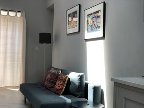 A modern living room with a sofa, two framed artworks, a floor lamp, and a window with curtains.