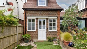 A small brick house with a white door, two windows, and a small garden with various plants and a lawn. - Wimbledon - Apartment - Sleeps 2 -private Entrance (London)